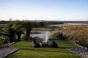 a fire pit in the grass next to a river at Hightide River Escape -with Outdoor Bath in Hokitika
