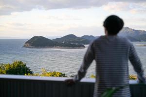 a man standing on a balcony looking out at the ocean at 父母ヶ浜リゾートヴィラ Senja in Mitoyo