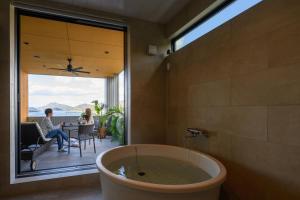 a bathroom with a tub and people sitting on a patio at 父母ヶ浜リゾートヴィラ Senja in Mitoyo