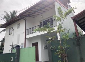 a white house with a green fence in front of it at Nirmalahomestay in Polgasowita