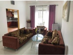 a living room with two couches and a glass table at Nirmalahomestay in Polgasowita +3 photos