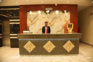 a man in a suit and tie standing behind a counter at Hotel Sahil Suites in Katra