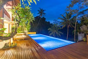 a backyard with a swimming pool and a wooden deck at River Sakti Ubud by Prasi in Ubud