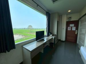 a room with a desk with a television and a large window at Chiang Rai Airport Hotel in Ban Fang Min