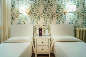 a bedroom with two beds and a wall with floral wallpaper at Hostal Cortés in Cuenca