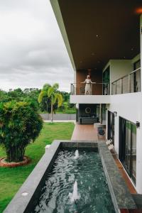 a person standing on the balcony of a house with a pond at Porsampao Luxury Villa in Ban Khok Khilek