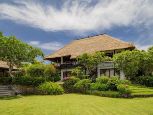 a house with a thatched roof and a yard at Radisson Blu Resort & Villas Bali Uluwatu in Uluwatu