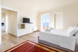 a white bedroom with a large bed and a tv at Hostdomus - Residenza La Vigna in Dogliani