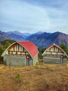two barns on a hill with mountains in the background at The Ridge Cottages - Sainj Valley in Sainj