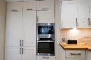a kitchen with white cabinets and a stainless steel oven at Roxby a stunning bungalow on the banks of the river within a 2 minute walk of Lake Ullswater and Pooley Bridge in Pooley Bridge +38 photos
