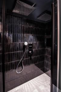 a black tiled bathroom with a shower with a hose at La Suite Bleue in Cholet