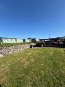 a field of grass with a stone wall and buildings at Caban Caru 2 in Tywyn