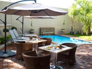 a patio with tables and chairs with an umbrella and a pool at Monte Bello Guesthouse in Windhoek +5 photos