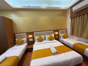 a room with three beds with yellow pillows at Hotel Sweet Inn in Mumbai