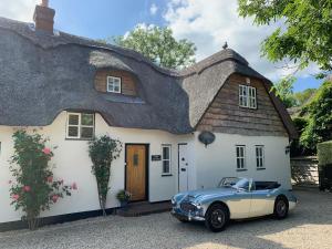 a car parked in front of a thatched house at Riverside Lodge Pied a Terre in Fordingbridge