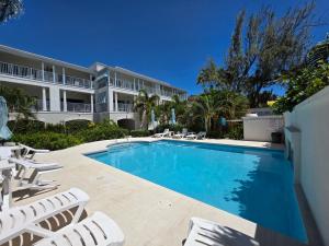 a swimming pool with chairs and a building at 102 Lighthouse Bay Barbados in Christ Church