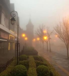 a foggy street with a building in the background with street lights at Pousada Folhas de Outono in Canela
