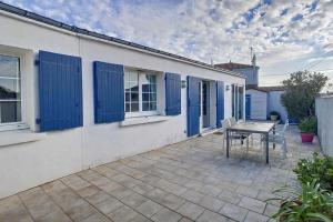 a patio with a table and blue shutters on a house at L'écrin des Ormeaux - sur l'île - 300 m de la plage in Barbâtre