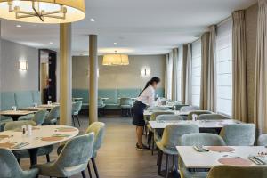 a woman standing in a dining room with tables and chairs at Hotel Aragon in Bruges
