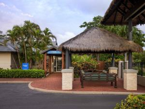 a bench in front of a building with a straw hut at Mantra Frangipani Broome in Broome