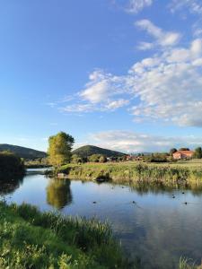 a river in a field with a blue sky and clouds at Studio apartman Vrba in Otočac