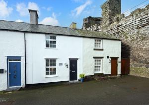 a white house with blue doors in front of a castle at Tŷ Gwyn Bach, Conwy in Conwy