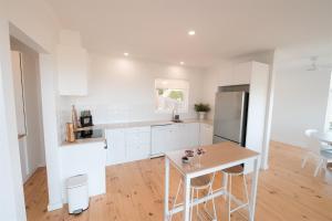 a white kitchen with a table and a refrigerator at Ocean Views Byron Infused Bliss NEW in Encounter Bay