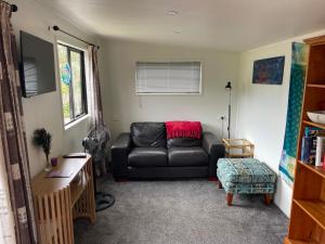 a living room with a black leather couch and a chair at Beach Bach Whangaumu Bay Tutukaka in Tutukaka