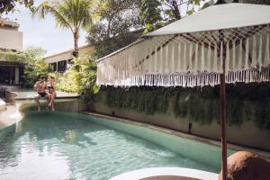 two women sitting on a wall next to a swimming pool at Sini Vie Resort & Spa Seminyak by Ini Vie Hospitality in Seminyak