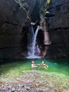 two people swimming in the water near a waterfall at Roseau Hostel & Beach Front Property in Roseau