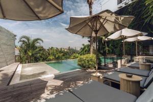a swimming pool with tables and umbrellas on a patio at Astera Resort & Spa Canggu by Ini Vie Hospitality in Canggu