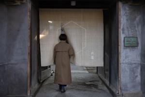 a man in a long coat looking at a drawing on a wall at Shirafuji in Suzaka