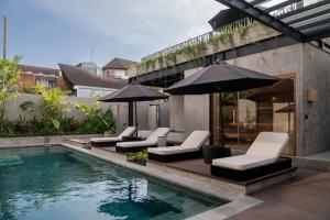 a pool with chairs and umbrellas next to a building at The Lario Collection - A Wellness Resort in Seminyak