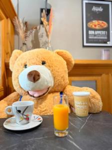 a teddy bear sitting at a table with orange juice at Brit Hotel Essentiel Reims Taissy in Reims