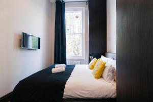Un dormitorio con una cama con almohadas amarillas y una ventana en The One Kensington en Londres