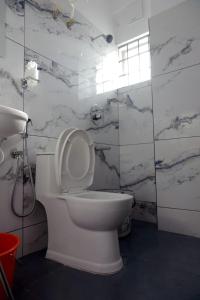 a white toilet in a bathroom with marble walls at Vaiga Heavens - 1 BHK Apartment, 500 m to temple in Guruvāyūr +12 photos