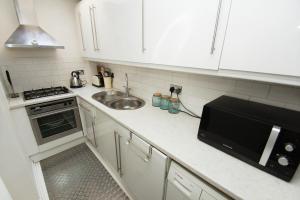 a kitchen with white cabinets and a sink and a microwave at Marine Gardens - Central - by Brighton Holiday Lets in Brighton & Hove