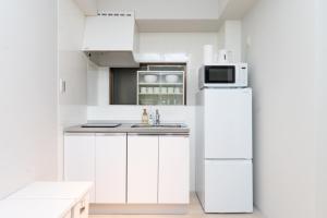 a white kitchen with a refrigerator and a microwave at Evergreen hotel yotsuya in Tokyo