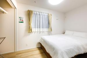 a white bedroom with a bed and a window at Anecis笠取町1 in Nagoya