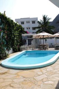 a swimming pool with an umbrella and tables and chairs at Nyumba Maua B&B in Watamu