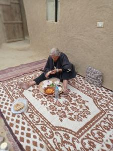 a woman sitting on the floor with a plate of food at Historical Mayor's House in Qasr Al Farafirah
