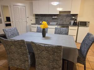 a dining room table with chairs and a vase with yellow flowers at Holiday Apartman in Kecskemét