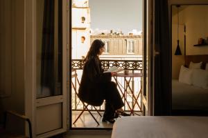 a woman sitting in a chair reading a book on a balcony at 9Hotel Bastille-Lyon in Paris