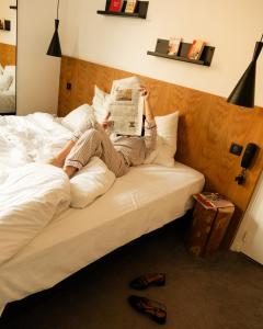 a woman laying on a bed reading a newspaper at 9Hotel Bastille-Lyon in Paris