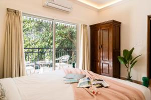 a bedroom with a bed with two books and a balcony at Staymaster Encanto - Serviced 2BHK in Siolim