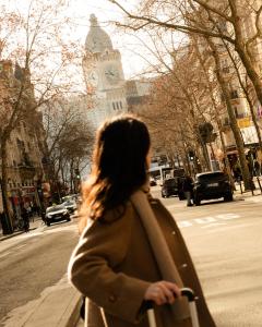 a woman walking down a city street with a clock tower at 9Hotel Bastille-Lyon in Paris