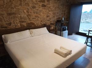 a bedroom with a white bed with a stone wall at Pensión A Lubre in Fisterra