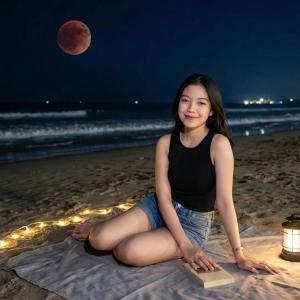 a woman sitting on the beach at night with the moon at Bandardarat in Manado