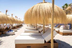 a row of beach chairs with straw umbrellas on the beach at Higuerón Hotel Málaga, Curio Collection by Hilton in Fuengirola
