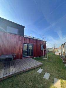 a red building with a wooden deck next to a yard at Kolokemp pri súkromnom jazere Boldog in Senec